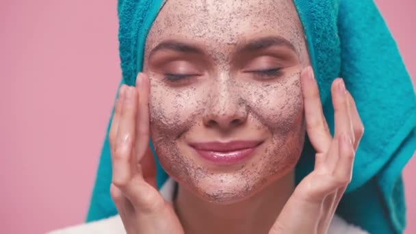 Mulher Feliz Com Toalha Cabeça Aplicando Esfoliação Facial Isolado Rosa — Vídeo de Stock