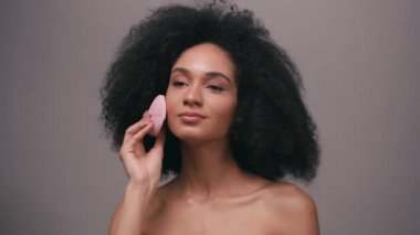 Siyahi Amerikalı kadın, silikon temizleyici kullanıyor. Yüzü ve boynu gri renkte.