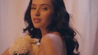 Saçlarını ayarlayan ve çiçekleri beyaz üzerine koyan kadının yavaş çekimleri 