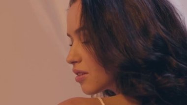 Kıvırcık saçlı esmer kadının beyaz kameraya baktığı ağır çekim.