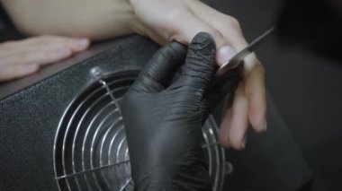 Manikürcü kadın tırnaklarını törpülüyor. 