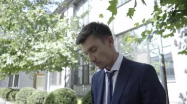 İşadamı dizüstü bilgisayar kullanıyor ve binanın yanındaki bankta oturuyor. 