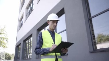 Açık havada yürürken panoya yazı yazan sert şapkalı bir inşaatçı 