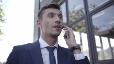 Takım elbiseli yönetici dışarıda cep telefonuyla konuşuyor. 