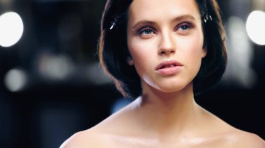 young model with bare shoulders and makeup looking away with back light on blurred background  clipart