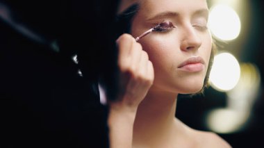 blurred makeup artist applying dark liquid eye shadow on eyelid of model  clipart