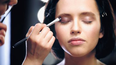 blurred makeup artist applying eye shadow with cosmetic brush on eyelids of model clipart