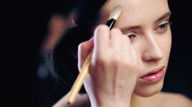 Bulanık makyaj sanatçısı kozmetik fırçalı genç bir kadının yüz hatlarını çiziyor.