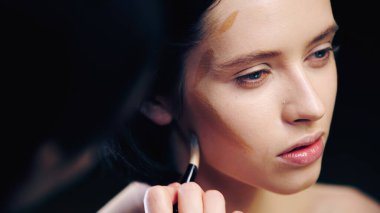 Bulanık makyaj sanatçısı kozmetik fırçayla modelin yüzünü şekillendiriyor.