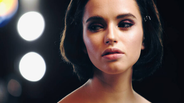 brunette woman with makeup looking away with back light on background