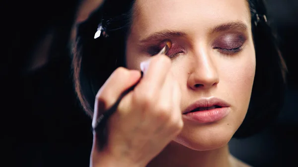 Visagistin Trägt Lidschatten Mit Kosmetikpinsel Auf Modell Mit Geschlossenen Augen — Stockfoto