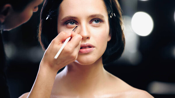 makeup artist applying eye shadow on lower eyelid of model with cosmetic brush