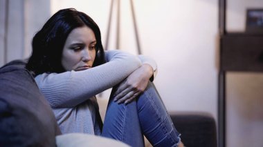 depresif bir kadın kanepeye oturmuş kendini kucaklıyor.