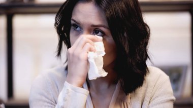 crying brunette woman wiping tears with paper napkin at home clipart