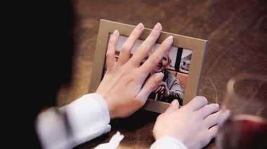 Kadın ellerinin evde yaşlı bir adamın fotoğrafıyla fotoğraf çerçevesine dokunuşunun kısmi görüntüsü