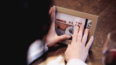 Evde gülümseyen yaşlı bir adamın fotoğrafıyla kadın ellerinin fotoğraf çerçevesine dokunuşunu kısmen görmek