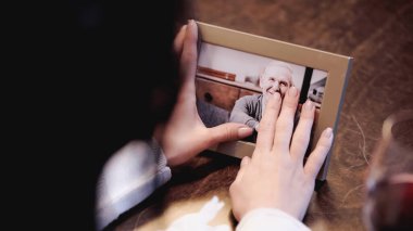 partial view of female hands touching photo frame with picture of smiling elderly man at home clipart