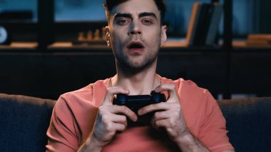 KYIV, UKRAINE - Haziran 09, 2021: şaşırmış adam elinde joystick ile evde video oyunu oynuyor 