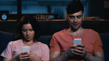 Modern oturma odasında cep telefonuyla mesajlaşan erkek ve kadın. 