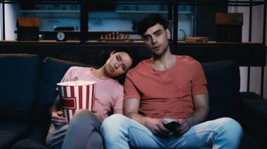 Uykulu kadın elinde patlamış mısır kovası tutarken ve film izlerken erkeğin omzuna yaslanırken.