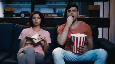Adam film izlerken karton kutuda Çin yemeği yiyen bir kadının yanında patlamış mısır yiyor.