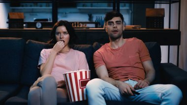 Kadın tuzlu patlamış mısır yiyor ve evde bir erkekle film izliyor.