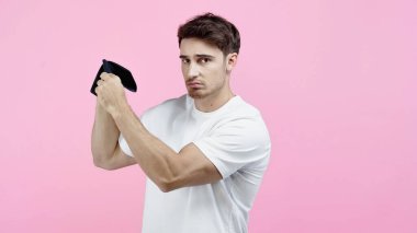 Upset man in white t-shirt holding empty wallet isolated on pink  clipart