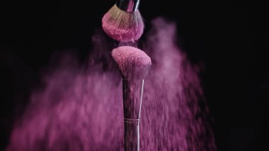 Siyah üzerine düşen pembe holi tozlu kozmetik fırçalar 