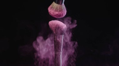 yumuşak kozmetik fırçalar siyah arka planda pembe holi boyaları serpiştiriyor