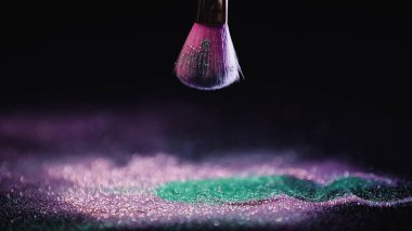 Siyah arka planda parlak pembe ve turkuaz tozların üzerinde kozmetik fırça