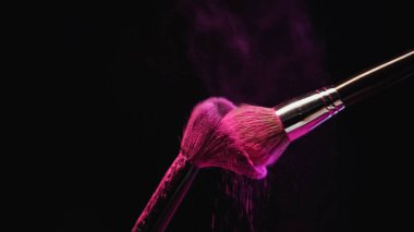 Parlak pembe holi tozlu kozmetik fırçalar siyah arkaplana vuruyor