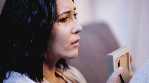 portrait of upset woman holding photo frame and crying on sofa at home