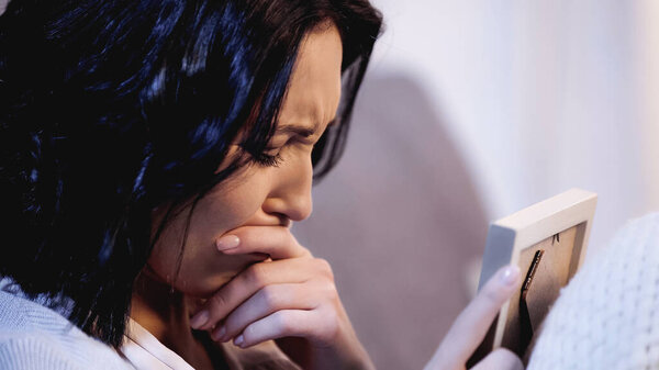 woman holding photo frame and crying with mouth covered with hand at home