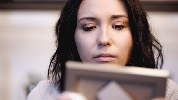 close up view of upset woman looking at photo frame photo frame at home