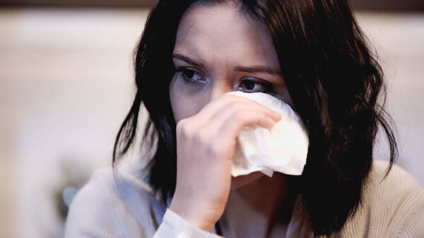 portrait of crying woman wiping tears with paper napkin at home
