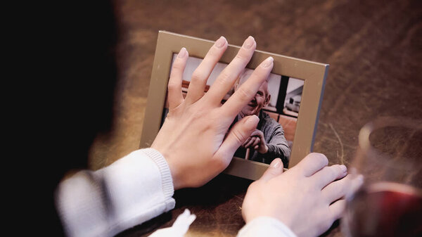 partial view of female hands touching photo frame with picture of elderly man at home