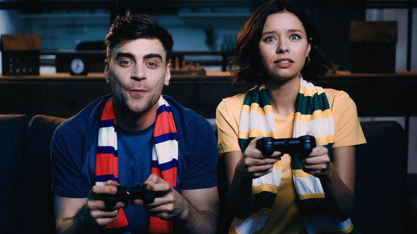KYIV, UKRAINE - JUNE 09, 2021: couple in striped scarfs holding joysticks and playing video game 