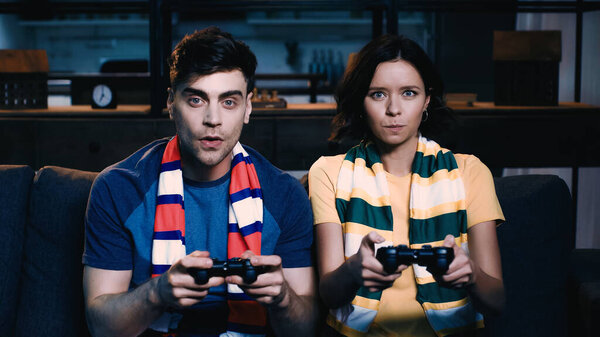 KYIV, UKRAINE - JUNE 09, 2021: man and woman in striped scarfs holding joysticks and playing video game 