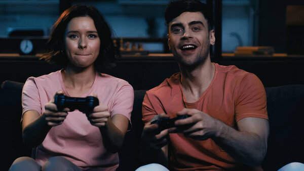 KYIV, UKRAINE - JUNE 09, 2021: tensed woman and happy man holding gamepads while playing video game 