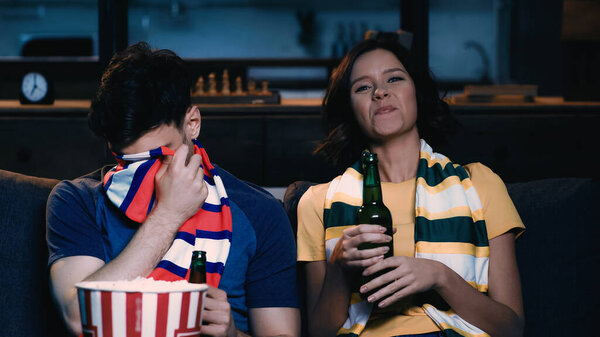 man covering face with scarf while watching championship with happy woman