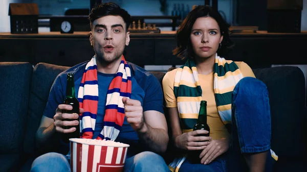 worried sport fans with scarfs sitting with bottles of beer and watching championship