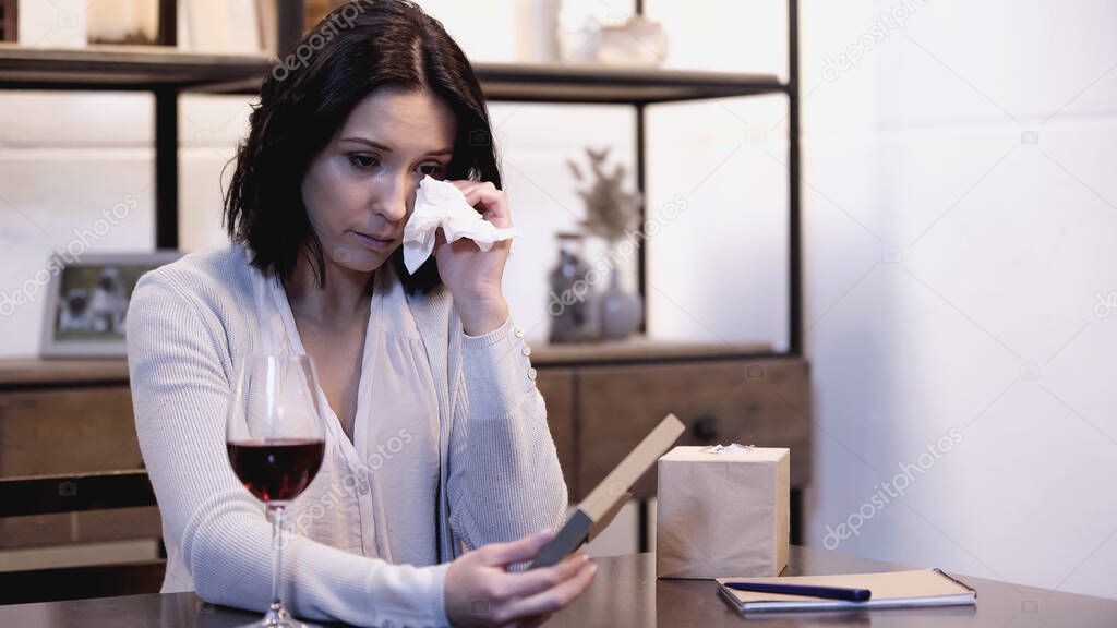 upset woman holding photo frame and wiping tears with paper napkin at home