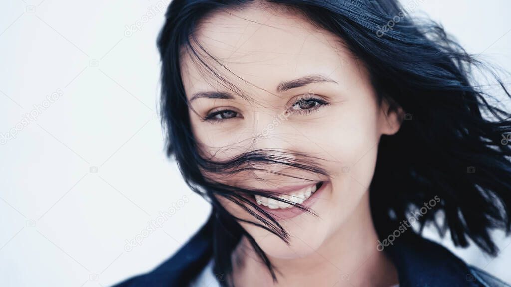 smiling woman with hair on wind covering face on grey background