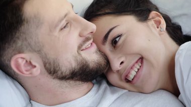 Yatakta dinlenirken sakallı sevgilisine yaslanan neşeli esmer kadın.