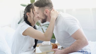 woman with braids kissing bearded man bringing breakfast in bed clipart