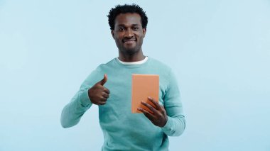Mutlu Afro-Amerikalı adam kitabı tutuyor ve mavi üzerine izole edilmiş bir şekilde parmağını gösteriyor.
