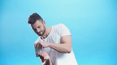 Cep telefonuyla video oyunu oynayan genç adam mavi ile izole edilmiş.