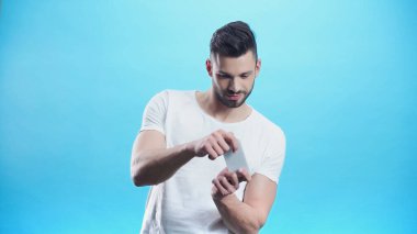 Cep telefonuyla oynayan genç adam mavi ile izole edilmiş.