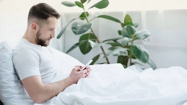 Jovem Barbudo Homem Usando Smartphone Cama — Fotografia de Stock