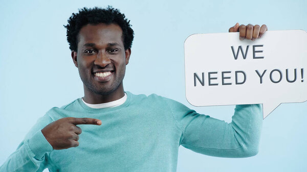 cheerful african american employer pointing at speech bubble with we need you lettering isolated on blue
